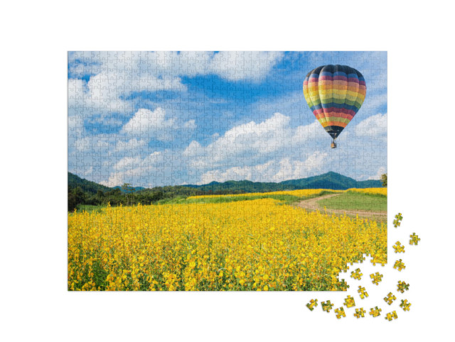 puzzle 1000 dílků „Horkovzdušný balón nad žlutými květinovými poli, v pozadí nízké pohoří“